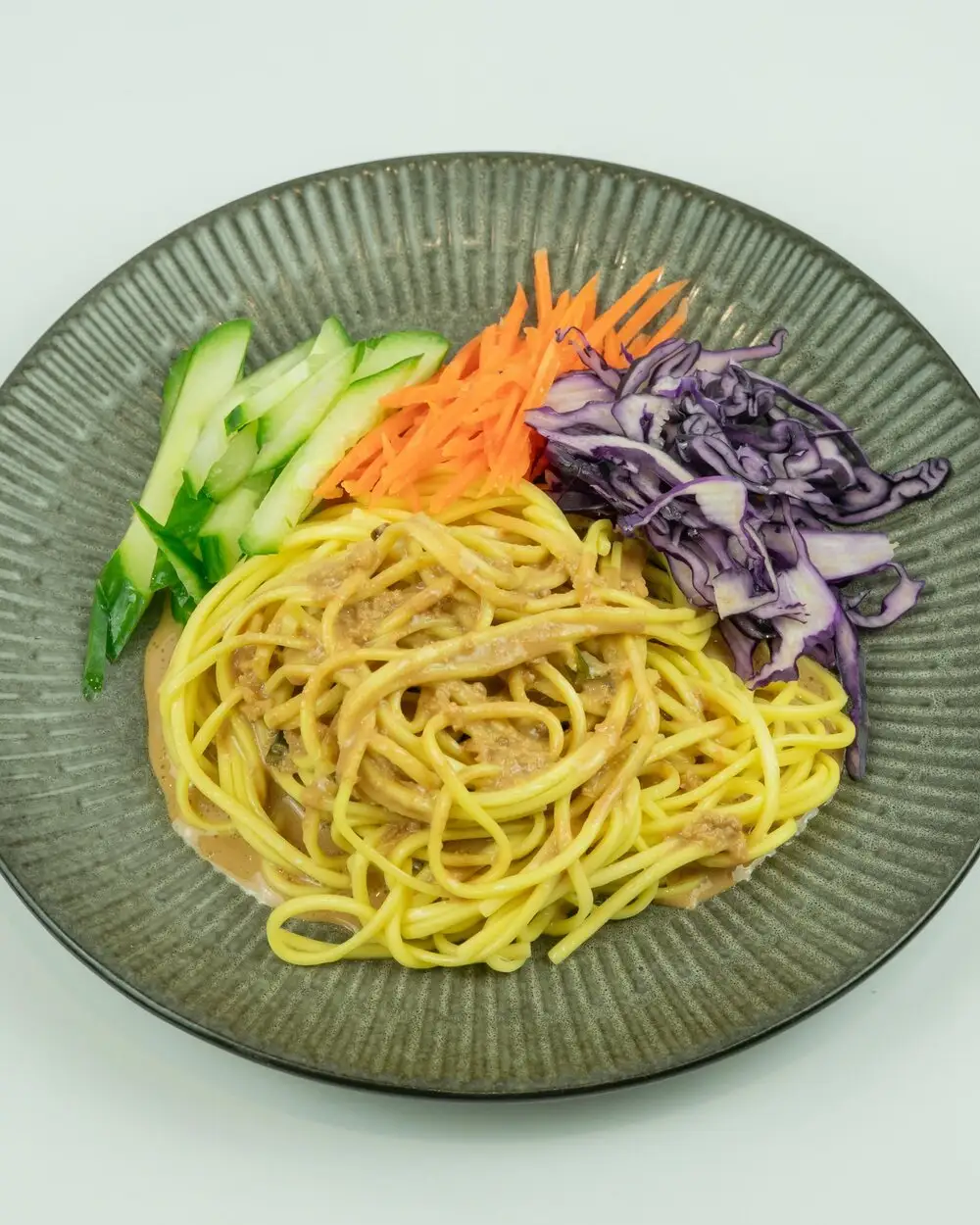 A plate of sesame noodle salad with shredded red cabbage, cucumber and carrot
